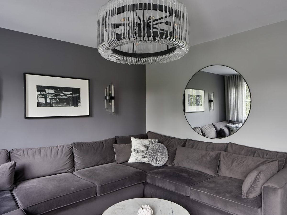 Sofa nỉ nhung xám chữ L lớn và gương tròn treo tường tạo chiều sâu không gian