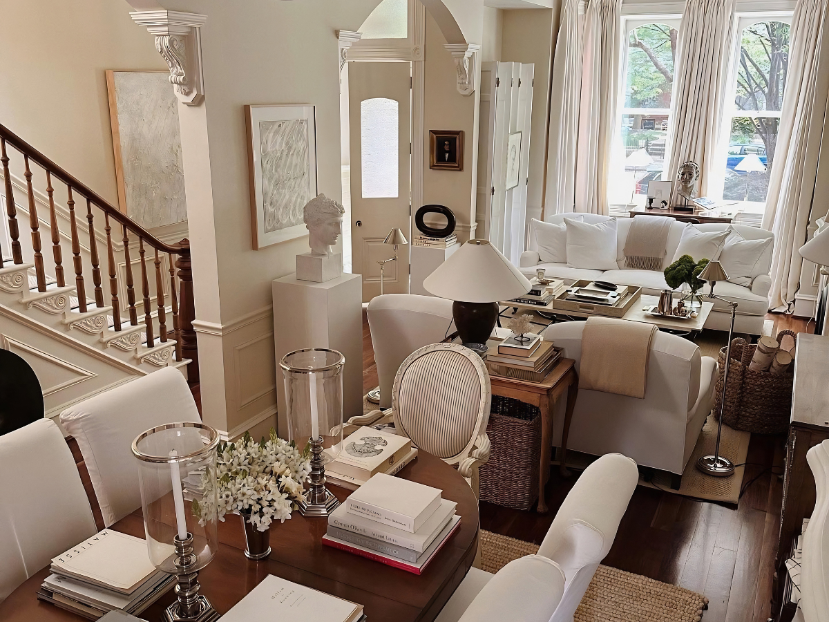 Thiết kế phòng khách nhà ống phong cách Tân cổ điển sang trọng với bộ sofa trắng, bàn trà trang trí sách và cầu thang gỗ truyền thống.