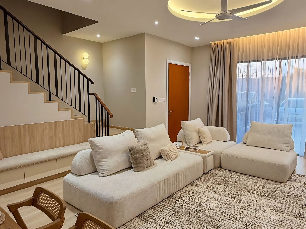 Mẫu thiết kế nội thất phòng khách nhà ống phong cách Tối giản với bộ sofa màu be cỡ lớn và kệ bục gỗ chạy dọc gầm cầu thang.